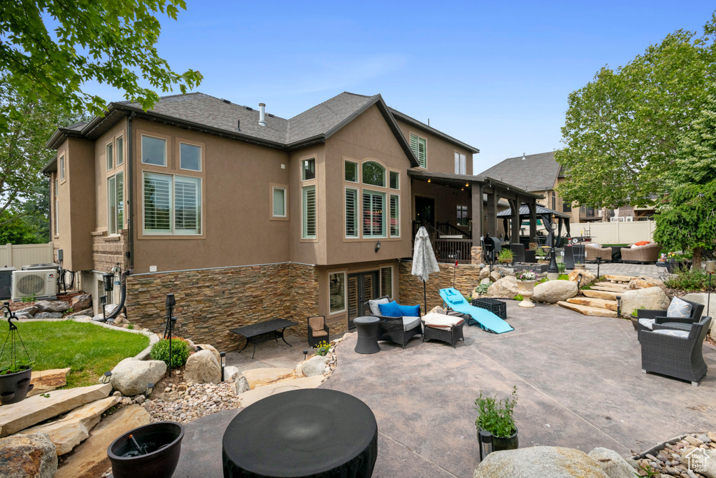 Back of house featuring stucco siding, a patio area, stone siding, a cooling unit, and an outdoor living space with a fire pit