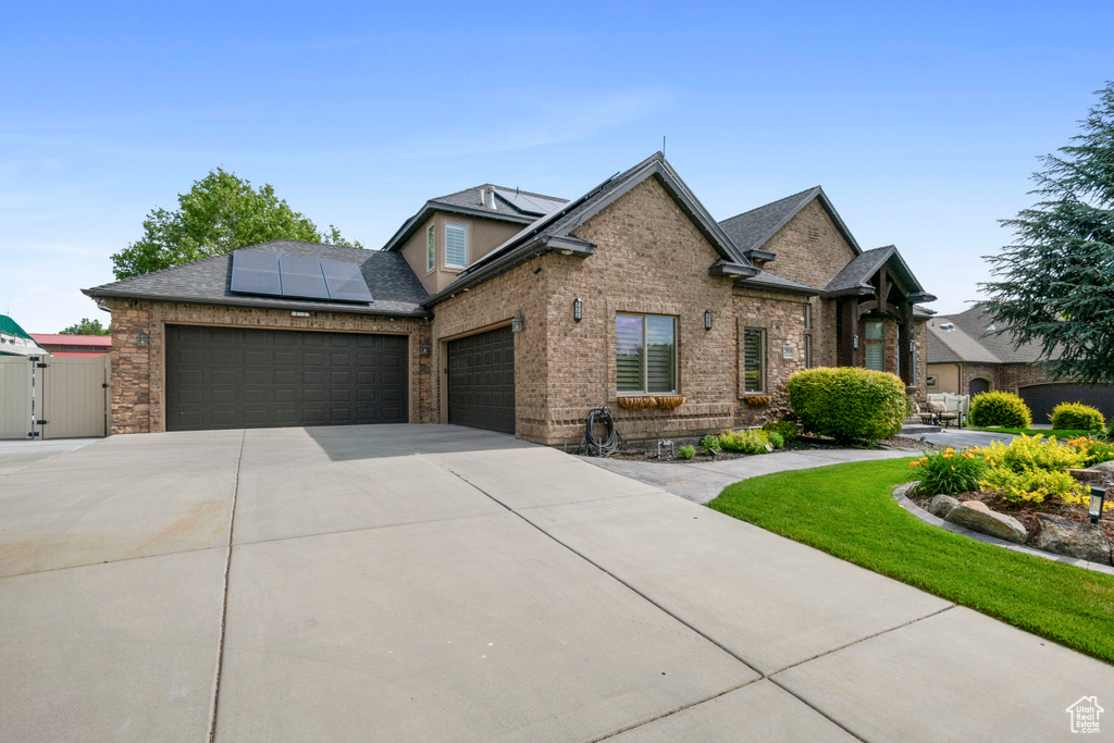 View of front of property with an attached garage, a gate, driveway, roof mounted solar panels, and brick siding