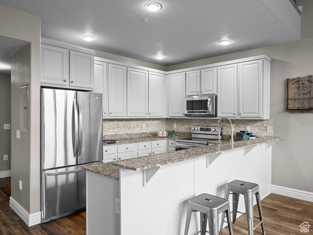 Kitchen featuring appliances with stainless steel finishes, a peninsula, baseboards, a breakfast bar area, and dark wood-style flooring