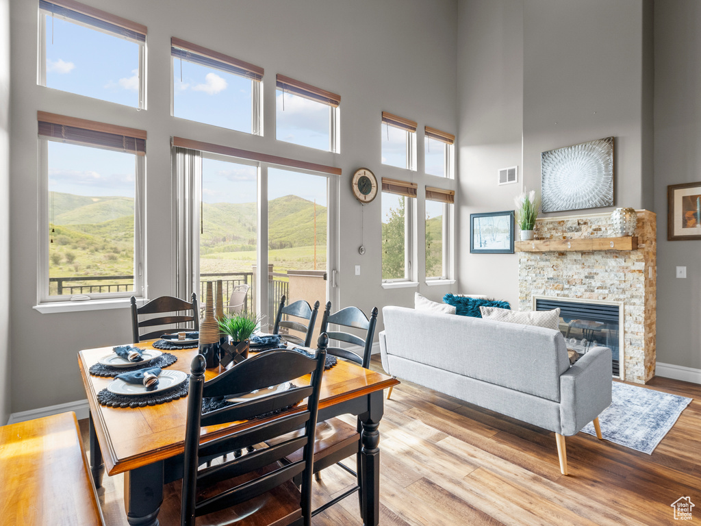 Dining space with a high ceiling, a stone fireplace, baseboards, and wood finished floors