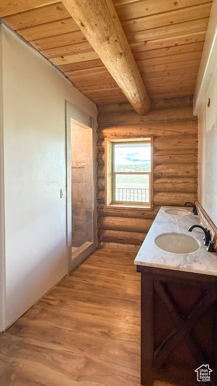 Bathroom with rustic walls, wooden ceiling with exposed beams, double vanity, and wood finished floors