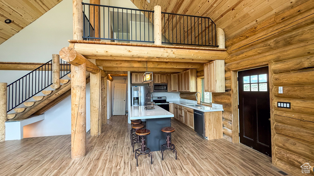 Kitchen featuring stainless steel appliances, a sink, high vaulted ceiling, light countertops, and rustic walls