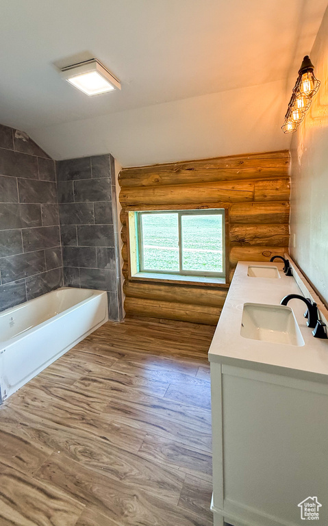 Full bath featuring log walls, double vanity, wood finished floors, lofted ceiling, and bathing tub / shower combination