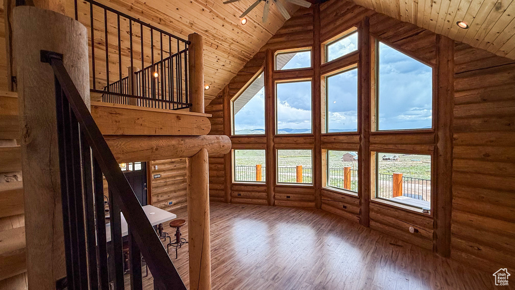 Unfurnished living room featuring high vaulted ceiling, hardwood / wood-style floors, log walls, wood ceiling, and a ceiling fan