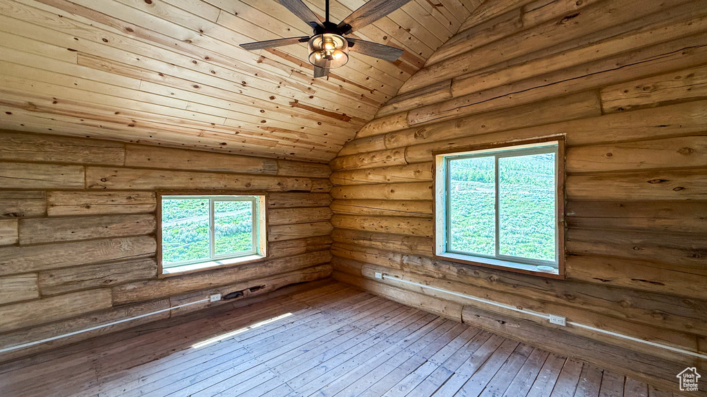 Empty room featuring ceiling fan, hardwood / wood-style floors, healthy amount of natural light, lofted ceiling, and rustic walls