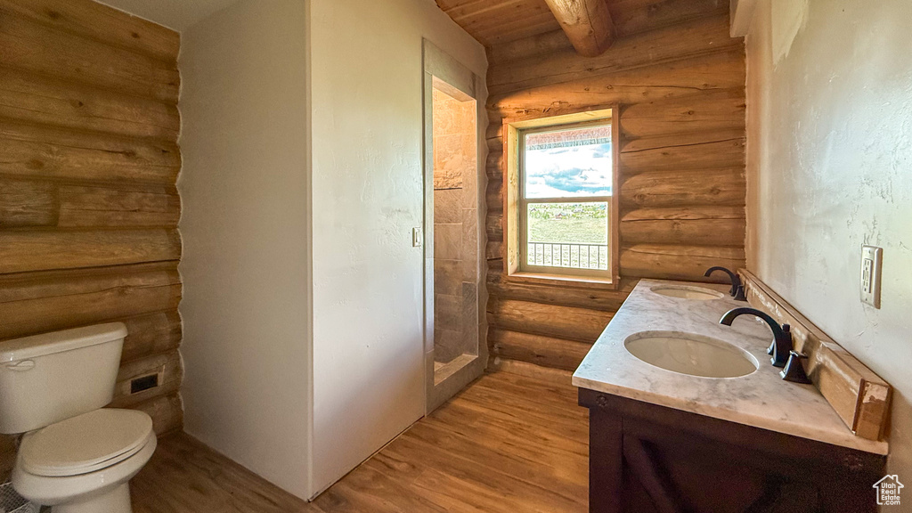 Full bathroom with rustic walls, wood finished floors, double vanity, toilet, and wood ceiling with exposed beams