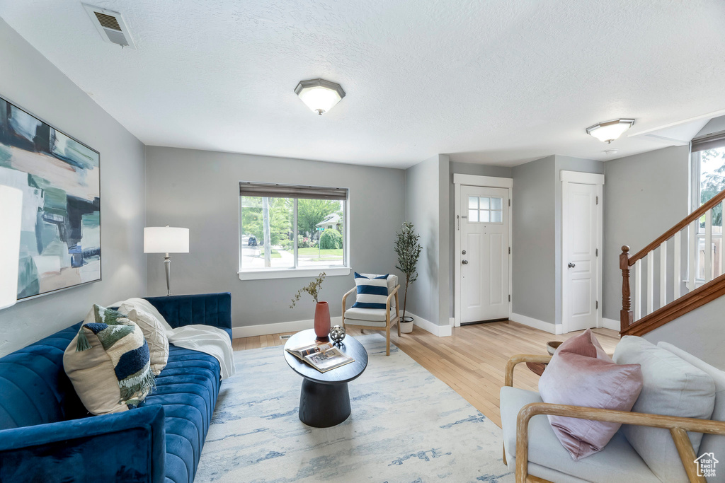 Living area featuring healthy amount of natural light, wood finished floors, baseboards, stairs, and a textured ceiling