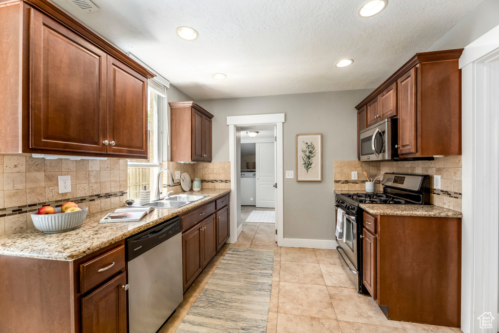Kitchen featuring appliances with stainless steel finishes, a sink, tasteful backsplash, washer / dryer, and recessed lighting