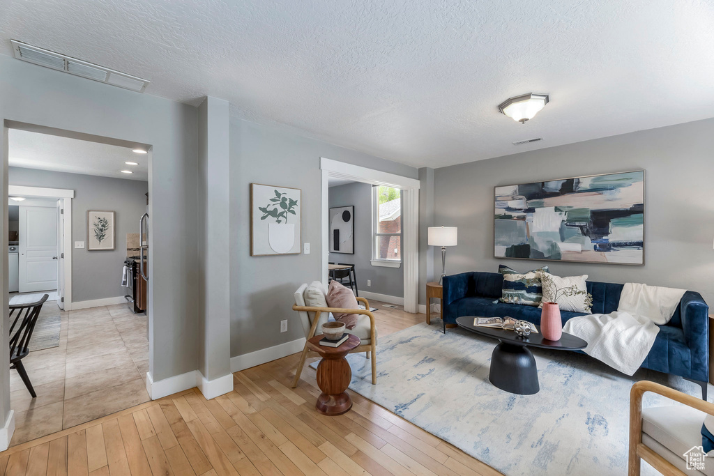 Living room with light wood finished floors, a textured ceiling, and baseboards