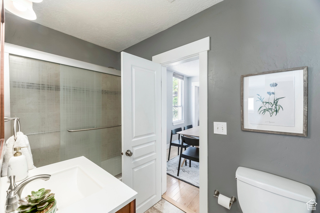 Full bath featuring vanity, toilet, wood finished floors, a textured ceiling, and a shower with door
