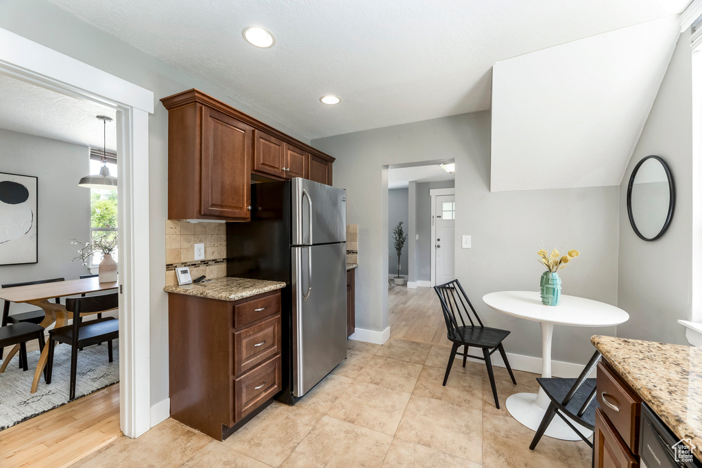 Kitchen featuring freestanding refrigerator, tasteful backsplash, light stone counters, baseboards, and recessed lighting