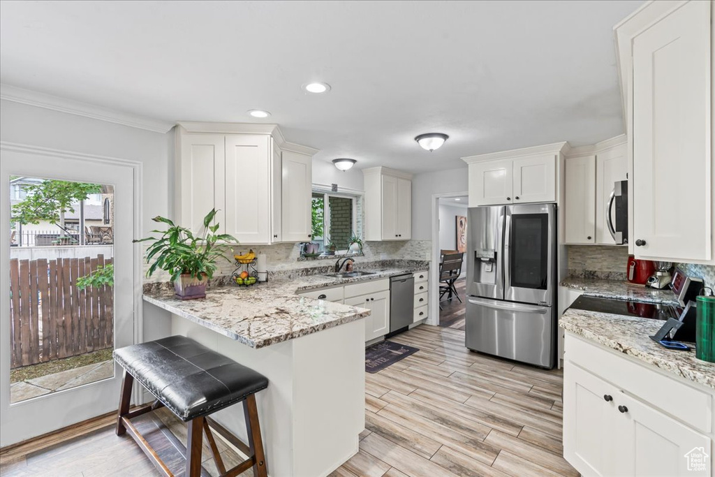 Kitchen featuring appliances with stainless steel finishes, backsplash, a peninsula, a kitchen breakfast bar, and recessed lighting