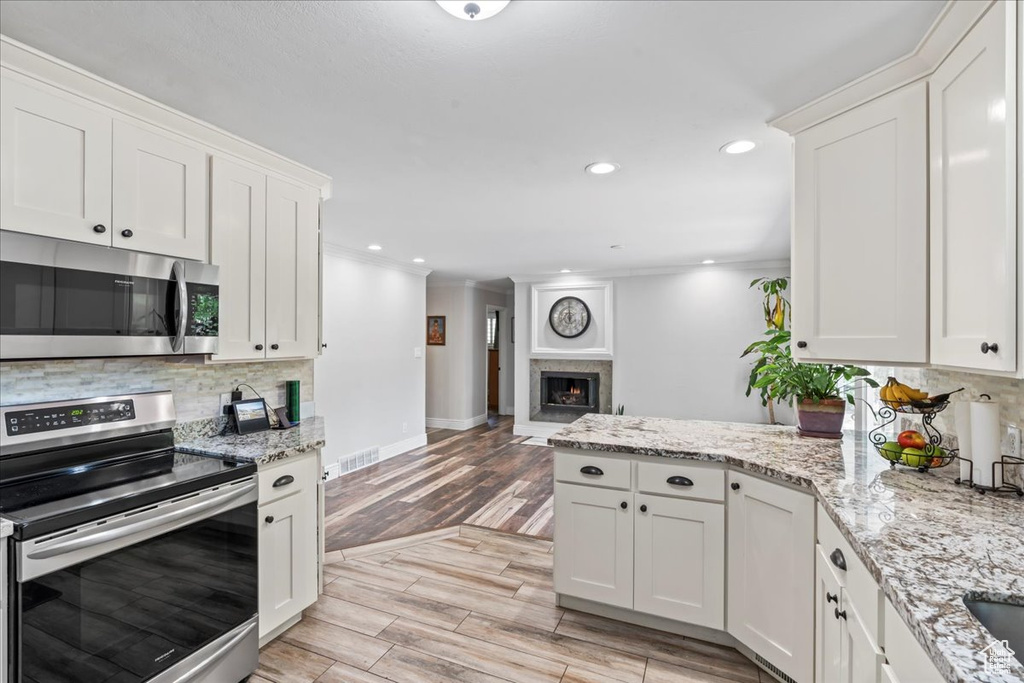 Kitchen featuring stainless steel appliances, backsplash, a peninsula, light wood-type flooring, and white cabinets