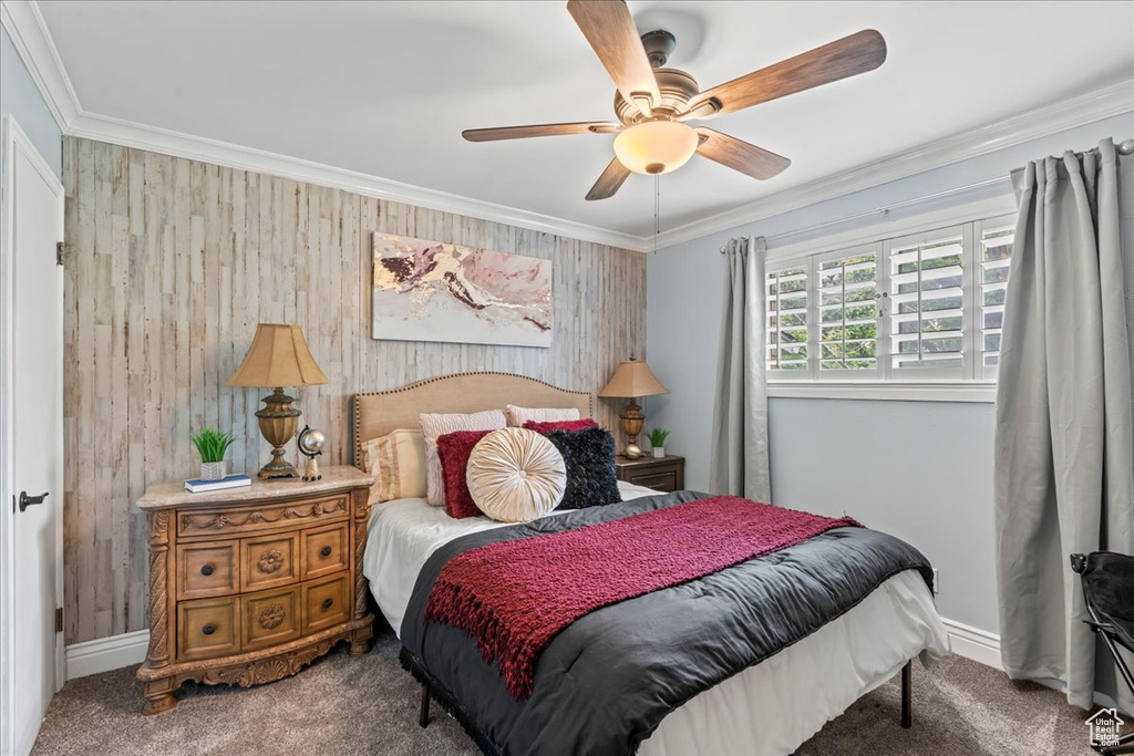 Carpeted bedroom featuring ornamental molding, wooden walls, baseboards, and a ceiling fan