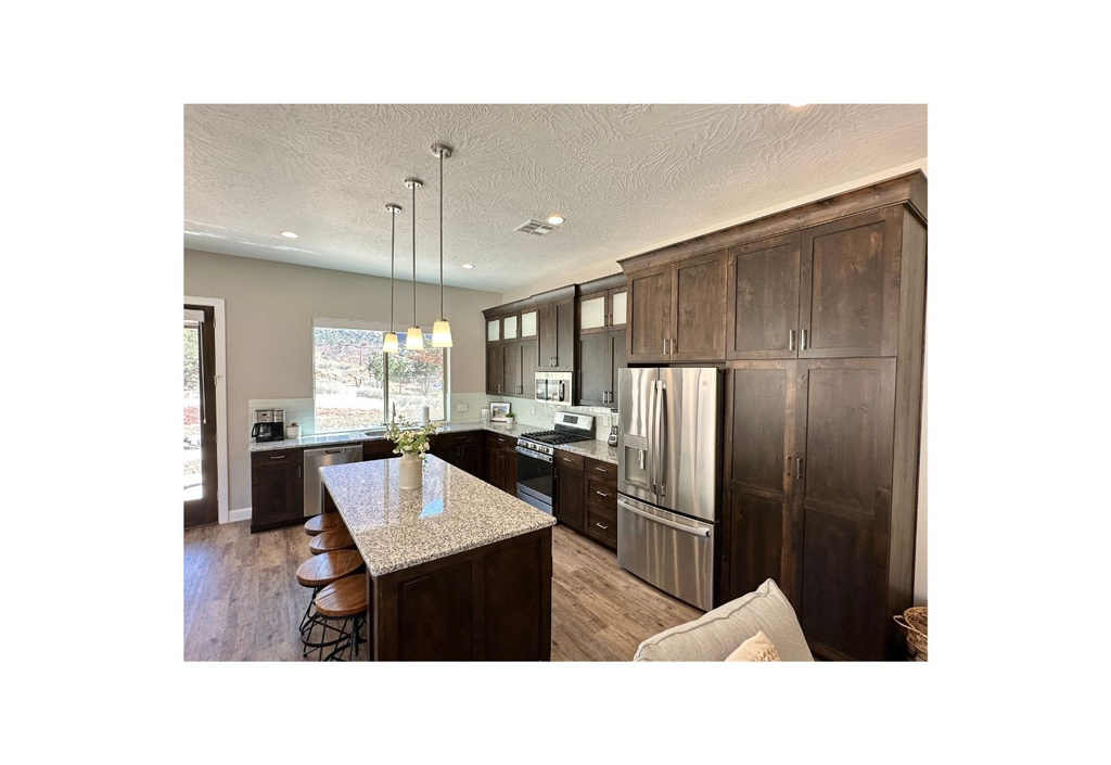 Kitchen featuring stainless steel appliances, a kitchen breakfast bar, dark brown cabinets, a kitchen island, and light wood-style floors