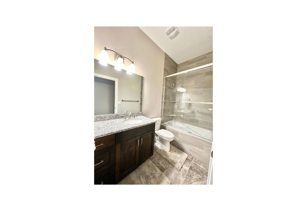 Full bath with toilet, vanity, and shower / bath combination with glass door