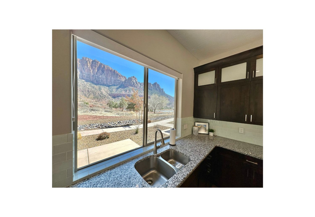 Kitchen featuring a sink, glass insert cabinets, light stone countertops, tasteful backsplash, and dark brown cabinets