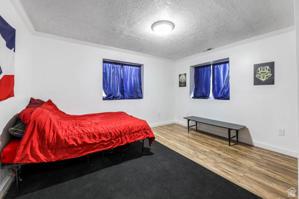 Bedroom with a textured ceiling, wood finished floors, crown molding, and baseboards