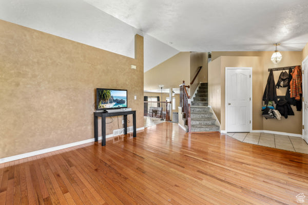 Unfurnished living room with wood finished floors, stairway, baseboards, and lofted ceiling