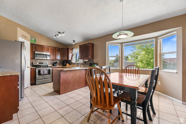 Dining space with light tile patterned floors, vaulted ceiling, and track lighting