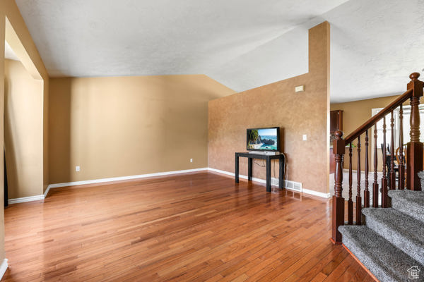 Unfurnished living room featuring wood finished floors, lofted ceiling, stairs, and baseboards