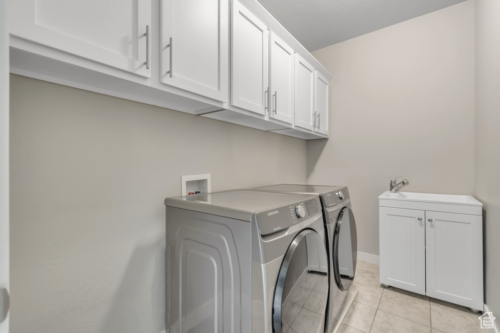 Washroom featuring cabinet space, washer and clothes dryer, light tile patterned floors, and baseboards