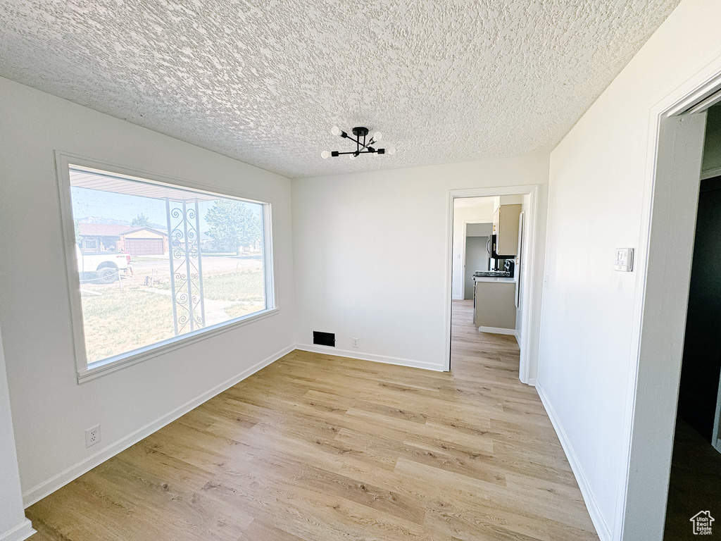 Unfurnished dining area featuring light wood-type flooring, a textured ceiling, and baseboards
