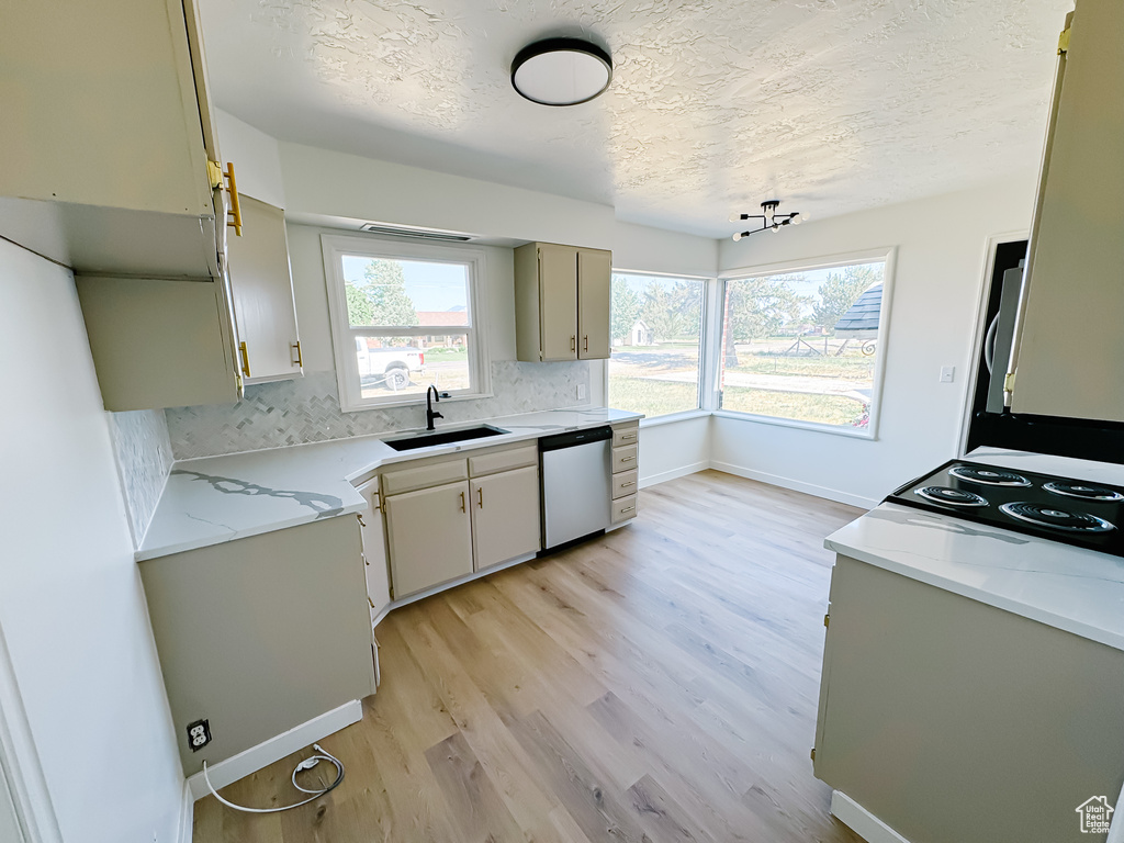 Kitchen with a sink, stainless steel dishwasher, a textured ceiling, light wood-style flooring, and decorative backsplash