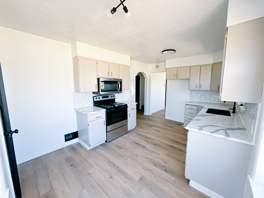 Kitchen featuring appliances with stainless steel finishes, decorative backsplash, arched walkways, light wood-style flooring, and a textured ceiling