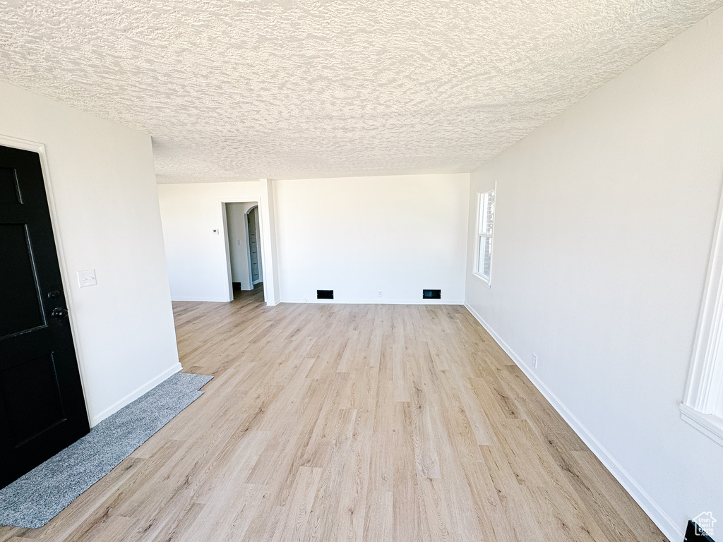 Empty room with light wood-type flooring, baseboards, and a textured ceiling