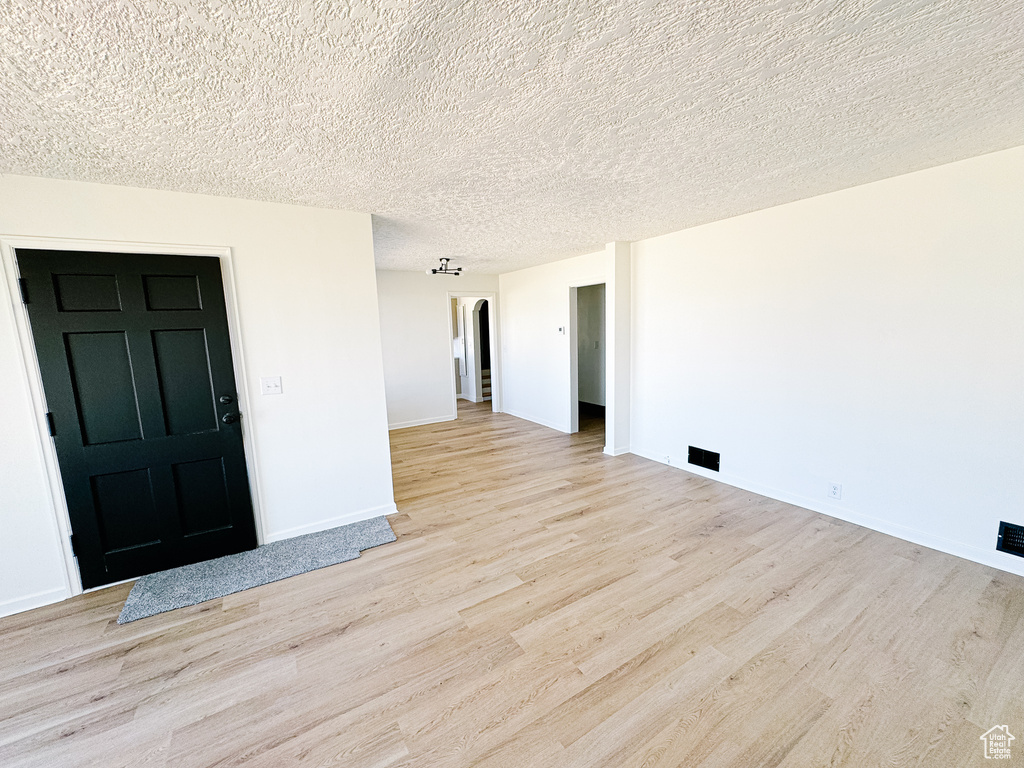 Empty room with light wood-style flooring, a textured ceiling, and baseboards