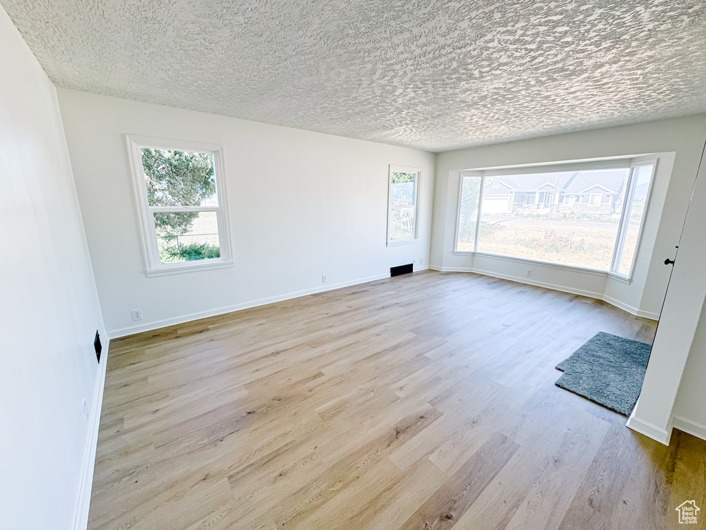 Spare room with wood finished floors, healthy amount of natural light, baseboards, and a textured ceiling