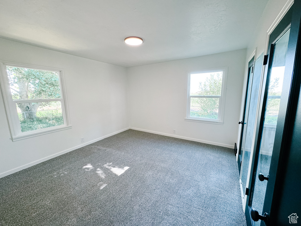 Unfurnished room featuring healthy amount of natural light, dark colored carpet, and baseboards
