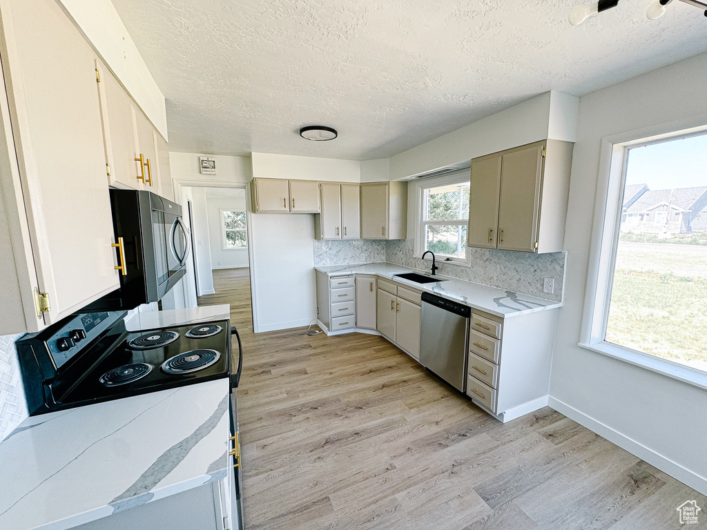 Kitchen featuring dishwasher, range with electric stovetop, a sink, a textured ceiling, and light wood finished floors