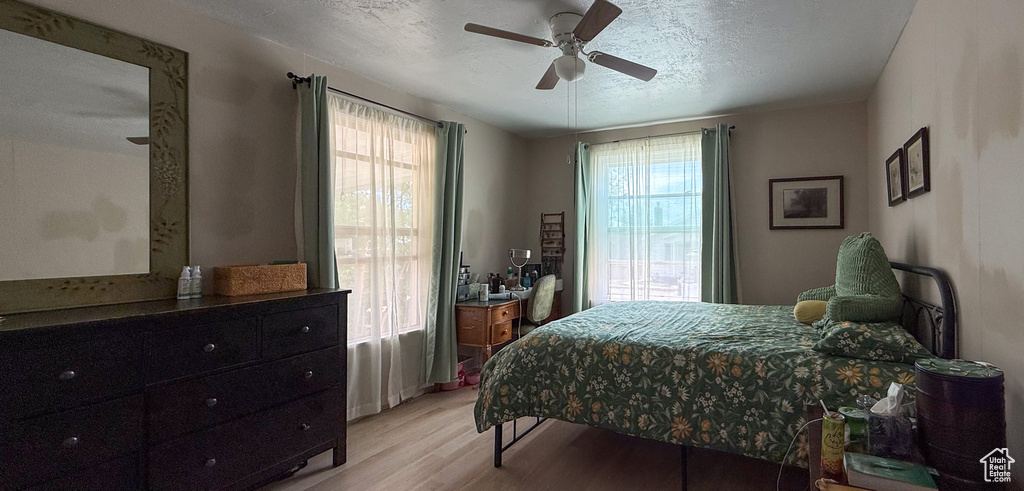 Bedroom with light wood finished floors, multiple windows, a ceiling fan, and a textured ceiling