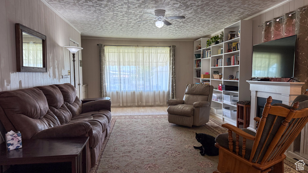 Living area featuring ceiling fan, crown molding, an ornate ceiling, a fireplace, and wood walls