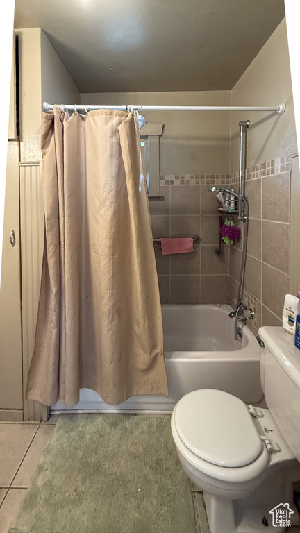 Bathroom featuring toilet, tile patterned flooring, shower / tub combo with curtain, and tile walls