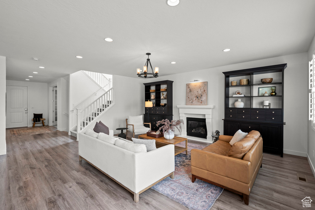 Living area with wood finished floors, a chandelier, a glass covered fireplace, recessed lighting, and stairway