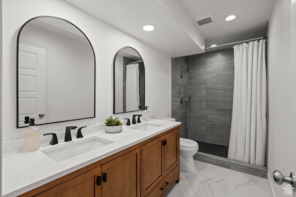 Full bath featuring recessed lighting, toilet, double vanity, marble finish flooring, and a tile shower