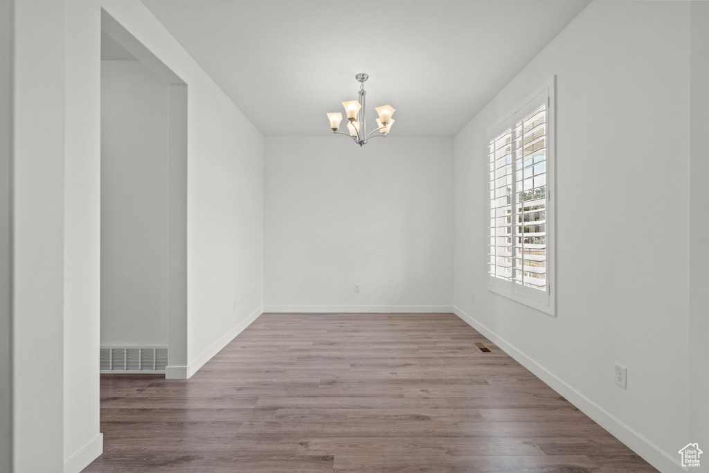 Unfurnished room featuring a chandelier, wood finished floors, and baseboards