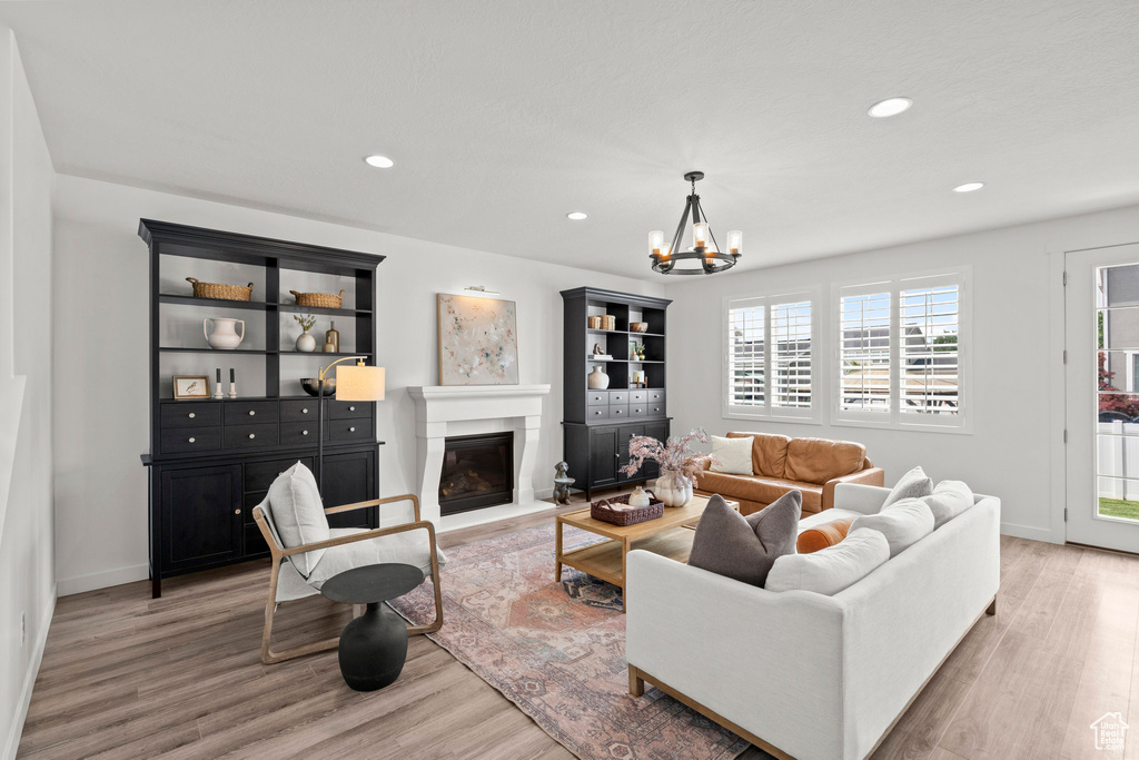 Living area with light wood-type flooring, a chandelier, a glass covered fireplace, recessed lighting, and baseboards