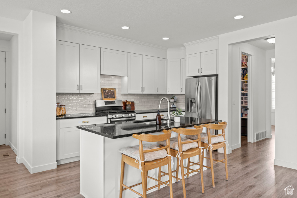 Kitchen with stainless steel appliances, a sink, a kitchen bar, light wood finished floors, and baseboards