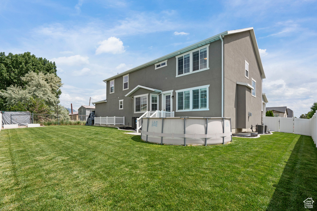 Rear view of property featuring stucco siding, central AC unit, and an outdoor pool