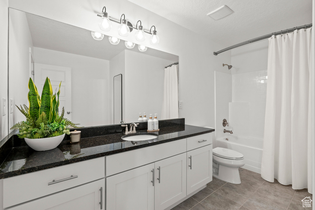 Full bathroom with double vanity, toilet, shower / tub combo, a textured ceiling, and tile patterned floors