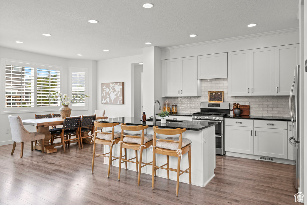 Kitchen with appliances with stainless steel finishes, dark countertops, a breakfast bar area, wood finished floors, and recessed lighting