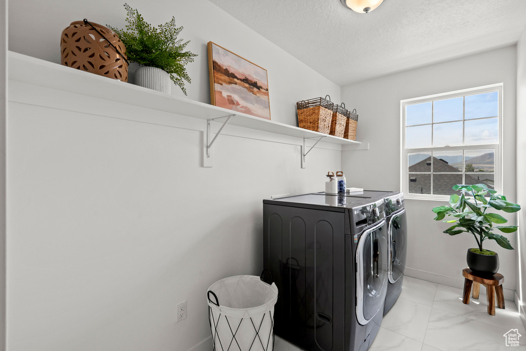 Laundry area featuring separate washer and dryer, light marble finish flooring, a textured ceiling, and baseboards