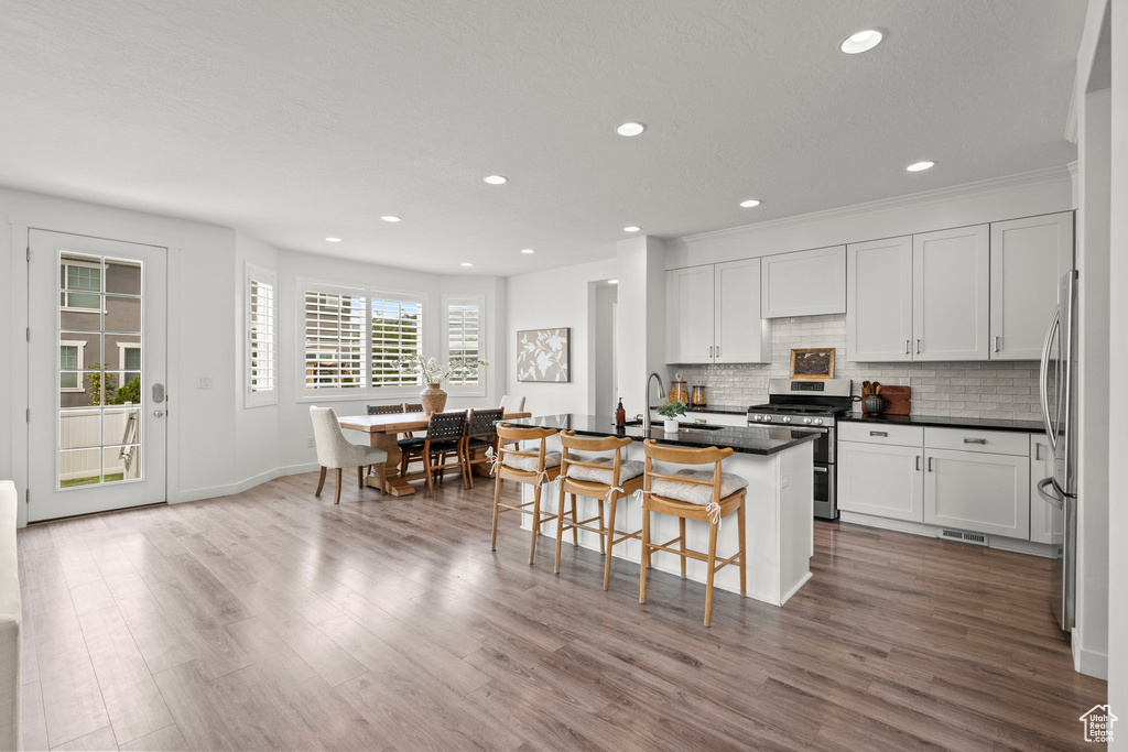 Kitchen with appliances with stainless steel finishes, dark countertops, a sink, tasteful backsplash, and a kitchen bar