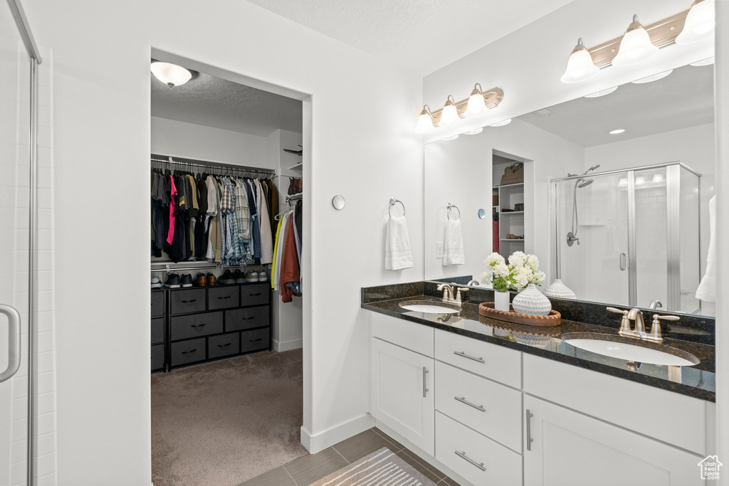 Full bathroom featuring a shower stall, a walk in closet, double vanity, baseboards, and tile patterned floors