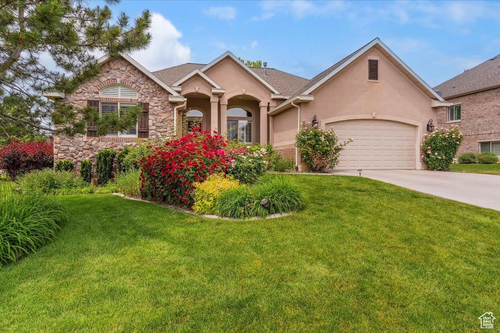 View of front of house featuring stucco siding, driveway, stone siding, and a front lawn