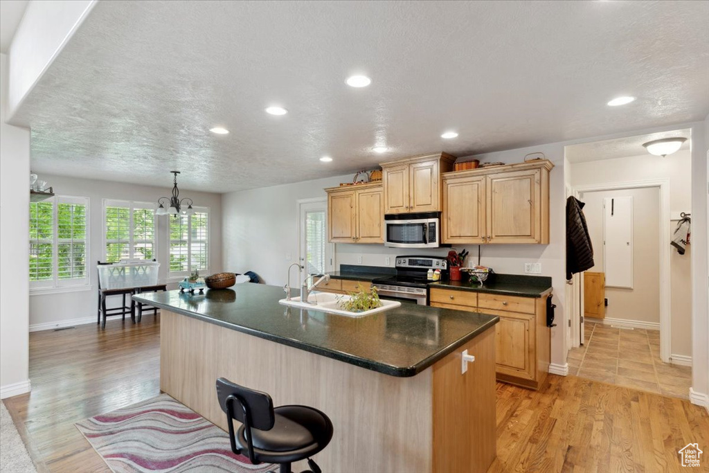 Kitchen with stainless steel appliances, light brown cabinets, dark countertops, a kitchen bar, and recessed lighting
